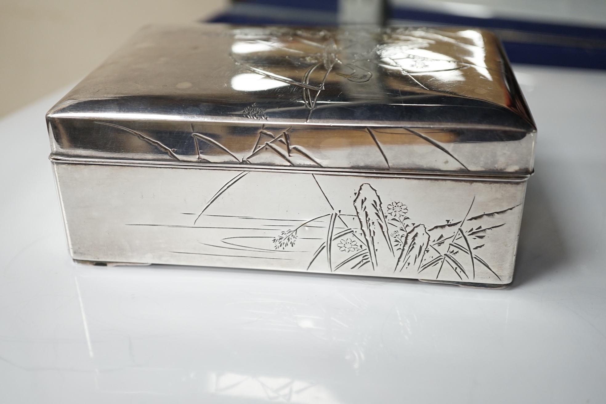 A Japanese white and yellow metal mounted rectangular cigarette box, engraved with birds and reeds, signed to the base, 14.2cm. Condition - fair